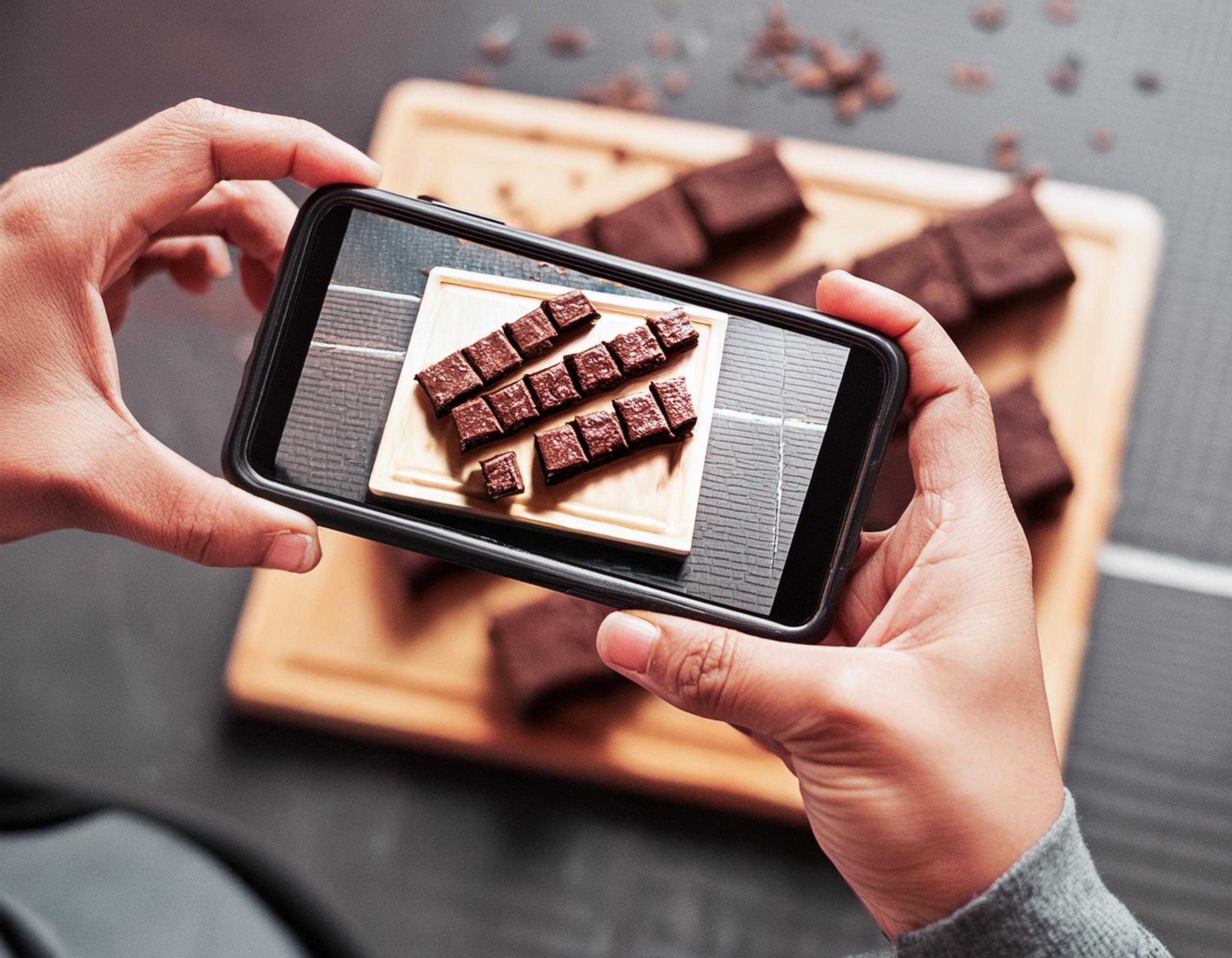 un homme avec un téléphone portable à la main prenant une photo d'un chocolat, vue d'en haut